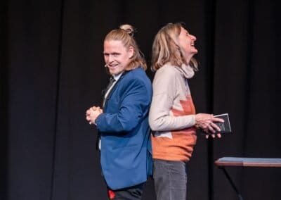 Henry Oz and a volunteer laughing back to back on stage during a comedy magic show in the San Juan Islands