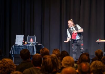 Henry Oz on stage with a red bag and Rubiks cube props during a comedy magic show in the San Juan Islands