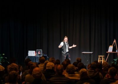 Henry Oz smiling with arms open welcoming the audience to a comedy magic show in the San Juan Islands